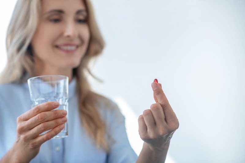 Dojrzała kobieta trzyma szklankę z wodą i tabletkę
