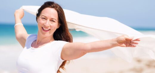 Ubrana na biało roześmiana dojrzała kobieta cieszy się letnią bryzą na plaży