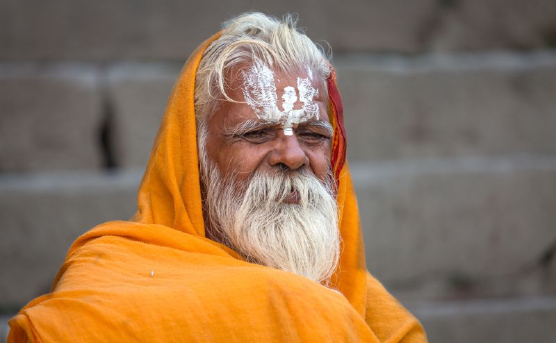 Siwy stary mnich z długą brodą owinięty w pomarańczową szatę.