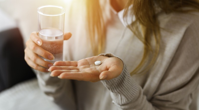 Kobiece dłonie trzymające szklankę z wodą i tabletkę