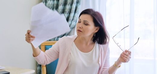 Dojrzała kobieta podczas uderzeń gorąca w menopauzie wachluje się kartkami papieru