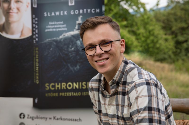 Autor Sławek Gortych na tle banneru ze zdjęciem jego książki “Schronisko, które przestało istnieć”